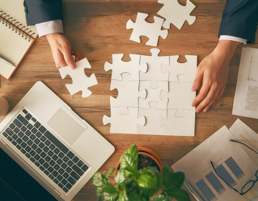 Man sitting at his workplace in the office. Top view close-up. Businessman is trying to connect couple puzzle piece. Symbol of association and connection. Concept of business strategy.